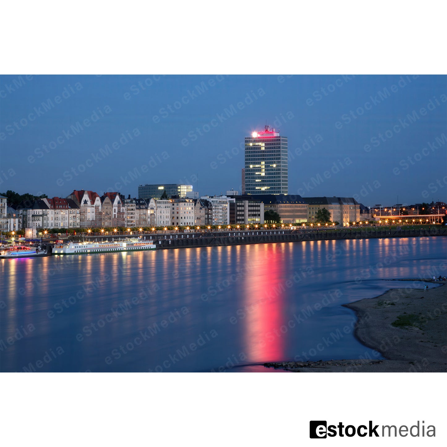 Düsseldorf waterfront at twilight with illuminated buildings and reflections on the Rhine River.