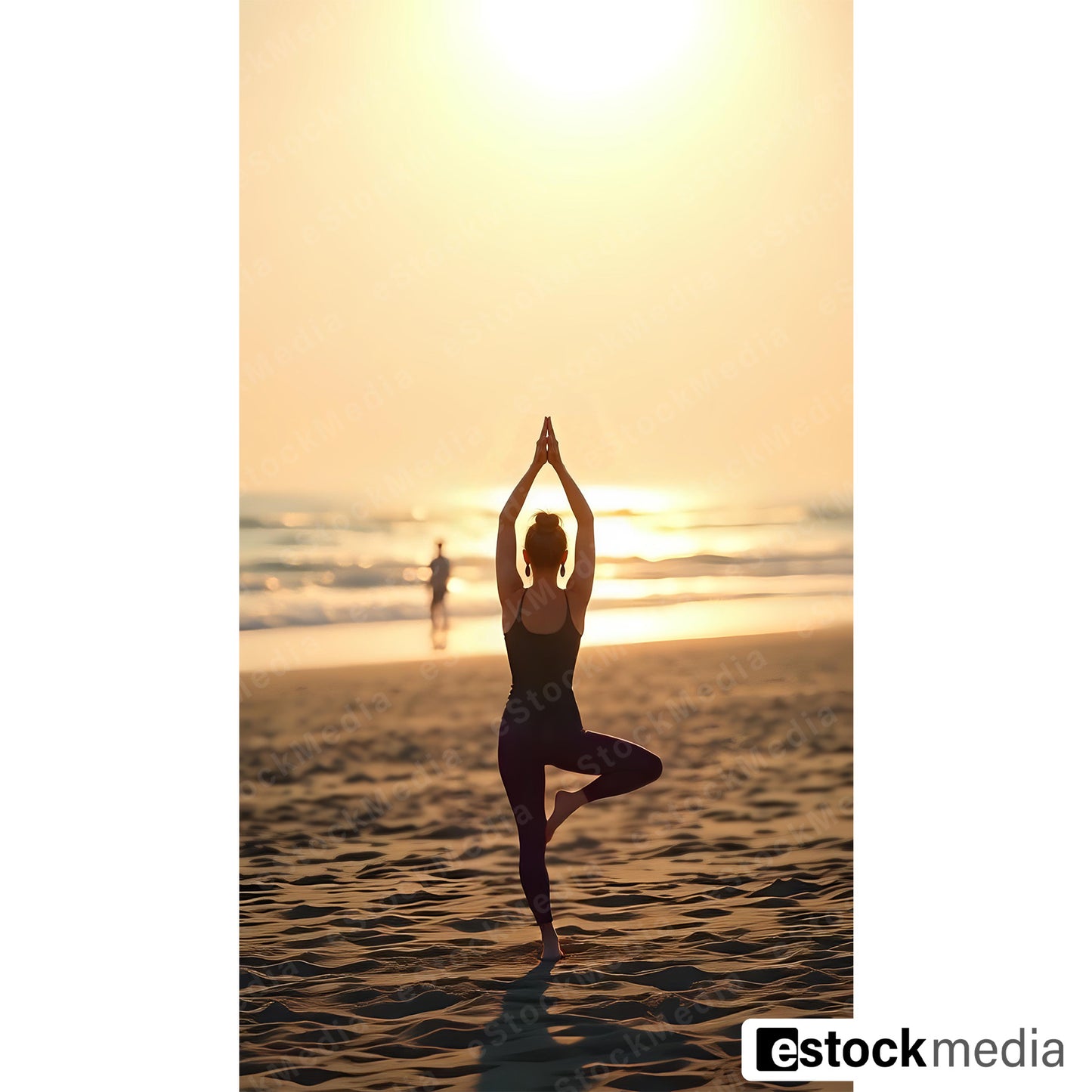 Woman with hair bun in dark sportswear doing tree pose yoga on sandy beach at golden sunset with ocean waves