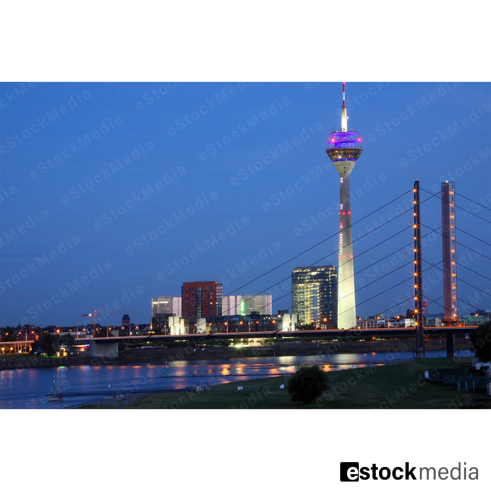 Illuminated Düsseldorf TV tower and bridge at night with reflections on the Rhine.