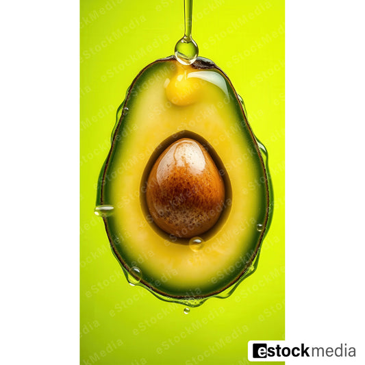 Halved avocado with creamy yellow-green flesh and brown pit catching a falling oil droplet against vivid green background.