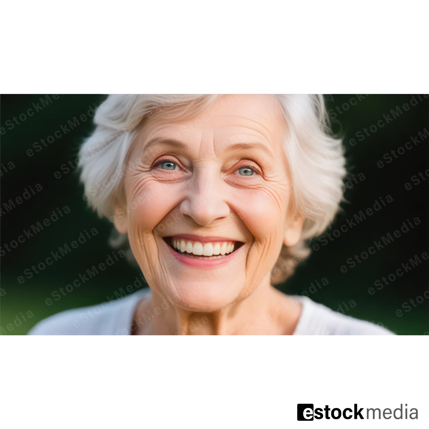 Close-up portrait of joyful elderly woman with short white wavy hair bright blue eyes and wide genuine smile wearing white top against softly blurred dark green bokeh background