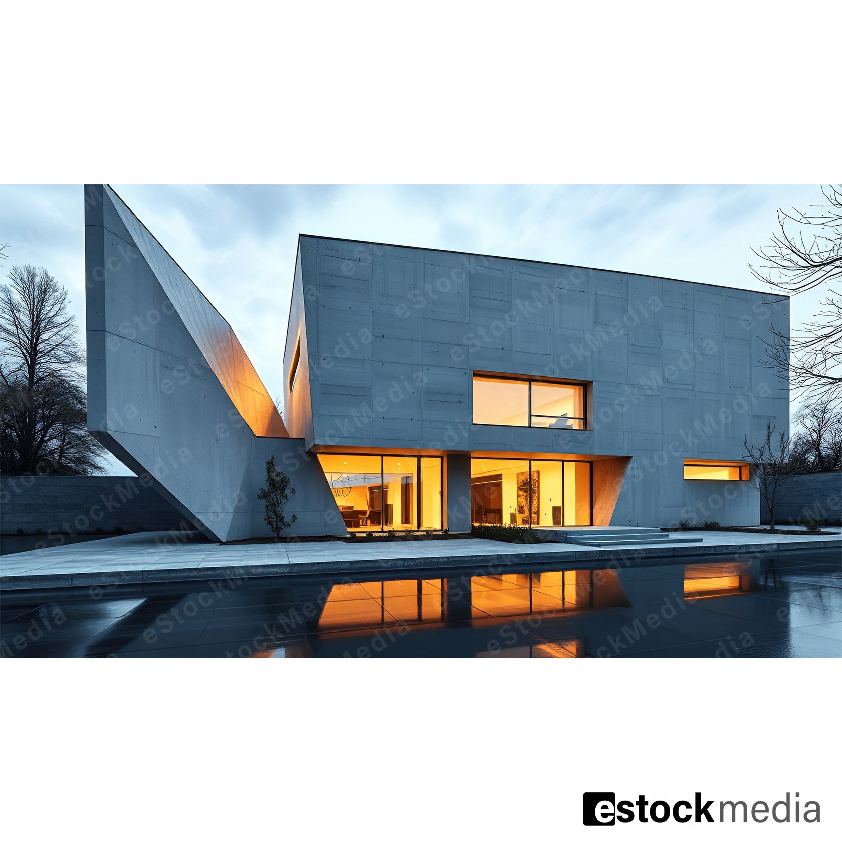 A modern concrete building with bold angular shapes and large glass windows, featuring warm interior lighting and a reflective water surface in front.