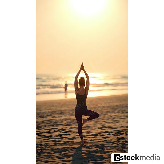 Woman with hair bun in dark sportswear doing tree pose yoga on sandy beach at golden sunset with ocean waves